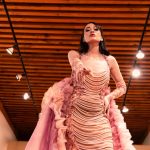 Modelo apresenta um vestido rosa em uma passarela de moda sob iluminação cênica.