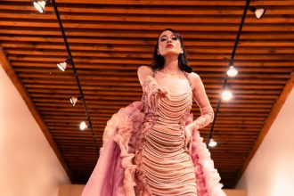 Modelo apresenta um vestido rosa em uma passarela de moda sob iluminação cênica.