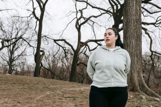 Mulher jovem com excesso de peso, usando roupa esportiva, se exercita em um parque arborizado.