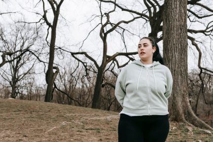 Mulher jovem com excesso de peso, usando roupa esportiva, se exercita em um parque arborizado.