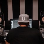 Produtor musical trabalha em um estúdio cercado por equipamentos de áudio.