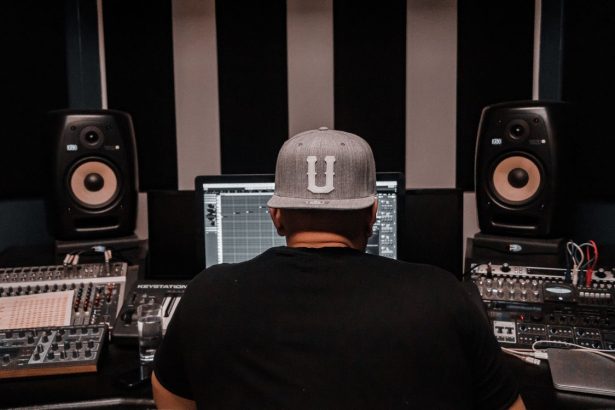 Produtor musical trabalha em um estúdio cercado por equipamentos de áudio.