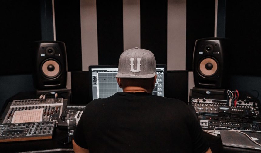 Produtor musical trabalha em um estúdio cercado por equipamentos de áudio.