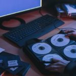Close-up de CDs e discos sobre uma mesa, com mãos em um ambiente tecnológico.