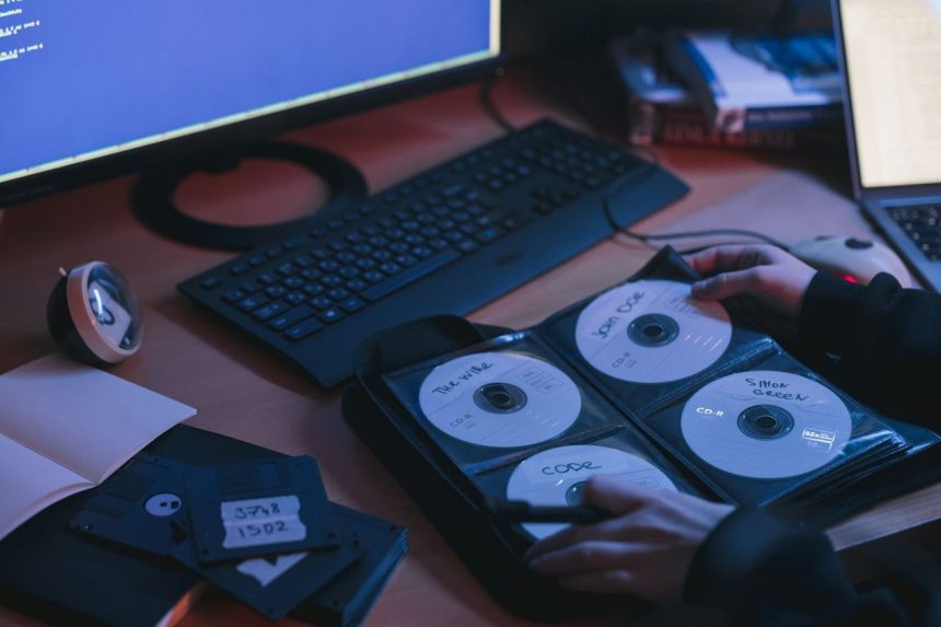 Close-up de CDs e discos sobre uma mesa, com mãos em um ambiente tecnológico.