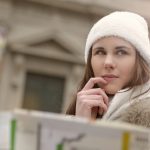 Mulher de casaco e gorro consulta um mapa em uma rua, procurando o caminho certo.